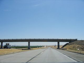 A service road for the canal crosses over the California 132 freeway. However, in the distance signs advise that the freeway section will briefly end and shift to a two-lane alignment.