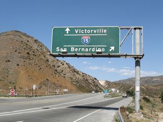A porcelain enamel sign, mounted over the eastbound lanes of California 138, provides guidance for motorists embarking onto Interstate 15. The first ramp connects to Interstate 15 south to San Bernardino, Riverside, and San Diego. The next left will connect to Interstate 15 north to Victorville, Barstow, and Las Vegas (at the stop sign).