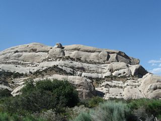 A prominent rock outcropping within the Cajon Pass/Cajon Summit area is Mormon Rocks, which are distinctive for their bald granite appearance and unique look amid the sagebrush-covered slopes. California 138 passes alongside the Mormon Rocks, then veers northwest toward Phelan.