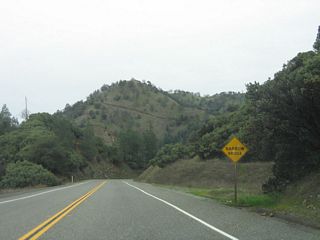 The approach to the suspension bridge is obscured as California 162 heads downhill and winds through several curves. A sharp turn north awaits at the bottom of the grade.