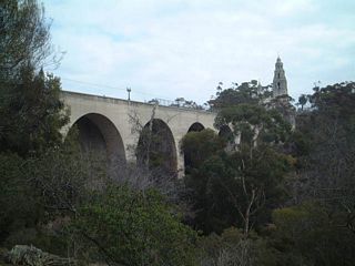 Looking northeast at the Cabrillo Bridge (Laurel Street Bridge) from a path in Balboa Park along the western frontage of the SR 163. The Cabrillo Bridge carries Laurel Street/El Prado over SR 163 (Cabrillo Freeway).