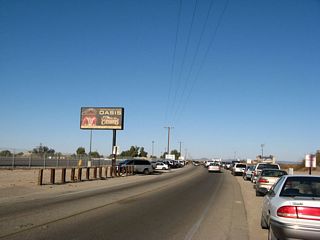 A billboard advertising for Quechan Indian Reservation's Paradise Casino is posted on the west side of California 186 (Algodones Road) as it travels north past cars parked along the highway. Despite "No Parking Any Time" signs on both sides of California 186, people frequently park alongside the state highway in order to avoid paying to park at one of the large parking lots on the west side of the highway in Andrade.