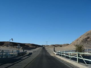 Original bridge railings carry the state highway over the All American Canal. White fences keep people away from the edge of the canal itself, which moves swiftly to the west as it travels toward the Imperial Valley. Drownings and other tragedies happen occasionally when people try to swim in or cross through the canals, not realizing the extent of the rapid current.