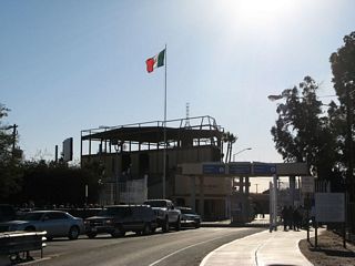 The Mexican flag flies over the Mexican side of the border crossing at the U.S.-Mexico border crossing. The border fence can be seen in the distance.