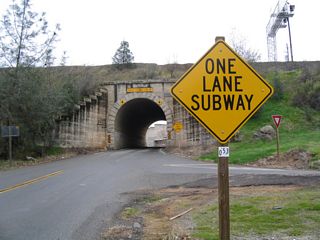 Old State Highway stems south from SR 193 (Newcastle Highway) at Main Street through a single lane tunnel below Southern Pacific Railroad tracks. The date stamp on top of the tunnel portal appears to be 1919.