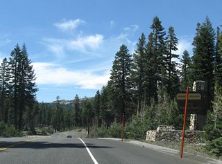 An Inyo National Forest sign greets visitors to Mammoth Mountain. Parking areas line both sides of the highway.