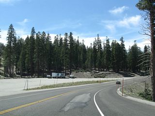 Westbound California 203 at the large parking area for Mammoth Mountain resort. Both sides of the highway feature perpendicular parking, and a large parking lot is located closer to the resort. During hours of shuttle operation, all through traffic to Devils Postpile and Reds Meadow must park and take the shuttle into the valley.
