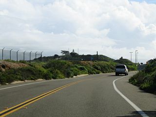 The lighthouse at Cabrillo National Monument comes into view along Cabrillo Memorial Drive south beyond Fort Rosecrans National Cemetery.