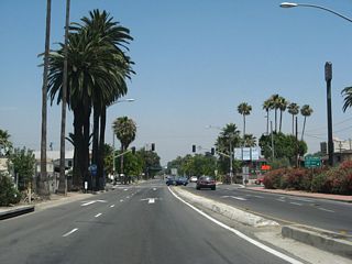 An odd configuration of two sets of one-way traffic converges (one set comes from Interstate 215 south, and the other comes from Interstate 215 north). The traffic signal ahead is configured to allow full movements from either set of lanes. Turn right for H Street south to California 66 (Fifth Street) west.