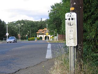 Two postmiles for unsigned California 222 are posted at the east end of the state highway: one on the north side of the street and another on the south side of the street for eastbound traffic. The gates of the monastery can be seen in the distance.