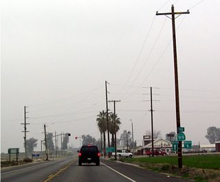 Westbound California 223 approaching California 99 Business, Union Avenue. The business route is old U.S. 99, and it can be seen from a distance due to the proximity of the eucalyptus trees that line the rural highway on both sides and in the median. On the trailblazer sign to California 99, note that no mention is made that Union Avenue (blinking red light) is the business route.