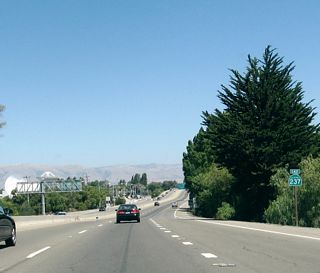A California 237 east reassurance shield is posted after the transition ramp from U.S. 101 south to California 237 east. Access to California 237 east from U.S. 101 north is provided via Mathilda Avenue. A few defense contractor satellite dishes can be seen in the background of this photo.