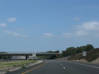 Curving through the Walnut Avenue interchange, California 261 sees a speed limit reduction. The toll road ends upon passing under the Walnut Avenue bridge (just ahead). Traffic from southbound Jamboree Road joins California 261 from the right; this will result in a widening of the freeway from two lanes to five lanes southbound.
