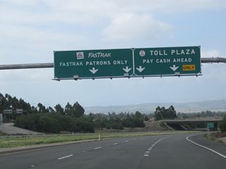 Through traffic on California 261 must pay a toll prior to the interchange with Irvine Boulevard. Stay left to use the FasTrak (electronic toll) lanes, or merge right for the cash toll plaza.