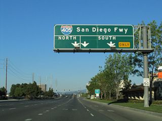 Northbound Jamboree Road approaches Interstate 405 (San Diego Freeway) at the upcoming folded diamond interchange. The first ramp connects to Interstate 405 south to San Diego, while the second ramp links to Interstate 405 north to Long Beach.