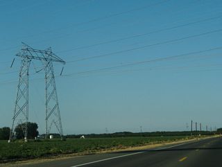 A set of transmission lines, including a 500kV power line that is part of Path 15, spans County Route E-6 ahead of Carmelo Way.