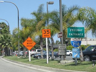 Leaving the Queen Mary and Cruise Ship Terminal within the Port of Long Beach, a freeway entrance shield assembly for Interstate 710 is posted along northbound Harbor Scenic Drive after the signalized intersection with Harbor Plaza, Queens Highway, and Harbor Scenic Drive.