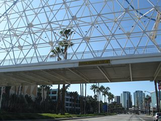 Beyond the traffic signal with Aquarium Way, Shoreline Drive passes under an elaborate pedestrian bridge that links The Pike shopping area on the north side of Shoreline Drive with the Aquarium of the Pacific on the south side of the roadway.