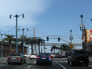 A pedestrian crossing is located at this traffic signal (Don Chee Way). The San Francisco-Oakland Bay Bridge comes into view and will dominate the view for the rest of the southbound trip along the Embarcadero.