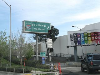 Southbound First Street approaches the on-ramp to the San Francisco-Oakland Bay Bridge crossing to Oakland and points east. This overhead sign is a rare back-lit guide sign that was likely placed in the 1960s-1970s time frame. This toll crossing entrance is located at the intersection between First Street and Harrison Street.