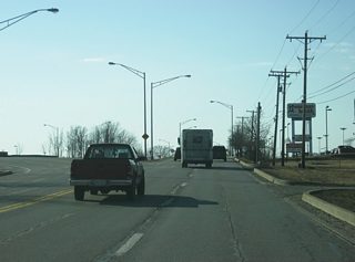 Illinois Road westbound continues west of Hillegas Road as the road splits again to serve the Jefferson Pointe shopping center. Two eastbound lanes from the Jefferson Pointe shopping center continue east on Illinois Road toward Hillegas Road.