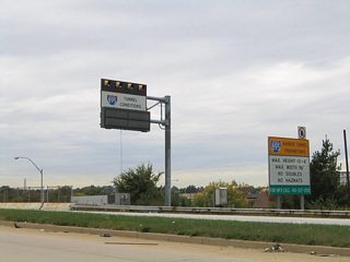 Looking back to the north, Moravia Road sees a loop ramp onto Interstate 895 (Harbor Tunnel Thruway) southbound for downtown Baltimore and Washington. A variable message sign and hazardous materials restrictions sign lie ahead of the freeway on-ramp.