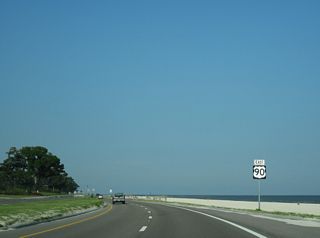 U.S. 90 rejoins its original alignment along Beach Boulevard east at 4th Avenue. 4th Avenue (Old U.S. 90) arcs west to Henderson Point from ahead of this reassurance marker.