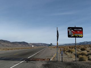 The Nevada welcome sign stands adjacent to the cattle guard and zero milepost marking the state boundary.