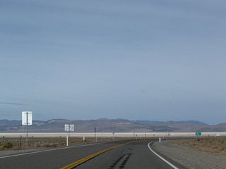 Several miles west of Nevada 265, U.S. 6 and U.S. 95 prepare to split at Coaldale Junction. This dramatic view shows the Columbus Salt Marsh, a huge dry lakebed located to the northwest of Coaldale that is mostly devoid of vegetation. The lakebed is the low point in the valley, and whatever precipitation runoff from neighboring mountains travels toward the lake. Due to the arid climate in the Great Basin, rainfall is uncommon, and thus the lakebed is mostly dry.