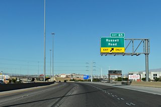 Interstate 11 curves westward ahead of Exit 65. Russell Road stretches eastward from the freeway to the site of Sam Boyd Stadium, former home of the University of Nevada at Las Vegas (UNLV) football team.