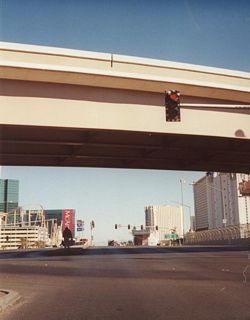 The left turn at the end of the overpass connects Tropicana Avenue east with I-15 north to Downtown Las Vegas and Salt Lake City. The Las Vegas Strip (former Nevada 604/Las Vegas Boulevard) is visible beyond I-15, as well as a view of the New York, New York hotel-casino to the north and Excalibur to the south. Tropicana Avenue has up to 12 lanes here including turn and auxiliary lanes.