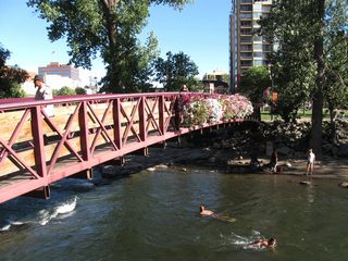 A rose-colored pedestrian bridge crosses the main channel of the Truckee River west of Sierra Street between the north bank and Wingfield Park, a large turfed park located on an island in the river.