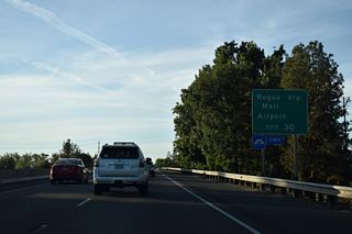 A grade separated intersection joins OR 62 (Crater Lake Highway) with parallel Biddle Road north to Rogue Valley International-Medford Airport (MFR). Rogue Valley Mall is west of I-5 adjacent to OR 99 (Riverside Avenue) northbound and OR 62. OR 99 southbound follows Court Street to Central Avenue.