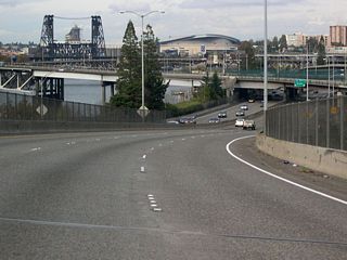 Moda (Rose Garden) Center appears in the distance where Interstate 5 lowers to grade level from the Marquam Bridge. Also appearing is the Steel Bridge, one of the only examples of a dual lift bridge in the world. Finished in 1912, the bridge's lower deck can be lifted independently of the upper deck.1
