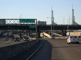 The Burnside Bridge (Burnside Street is Portland's north-south divider arterial) spans Interstate 5 north in this scene. The elevated lanes ferrying traffic to and from I-84 parallel this stretch. Spires of the Oregon Convention Center rise along the east side.
