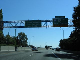 Spires of the Oregon Convention Center appear along the east side of the Interstate 5 where the entrance ramp from Wheeler Avenue and Winning Way adds an auxiliary lane to Exit 301 for I-84/U.S. 30 east. 
