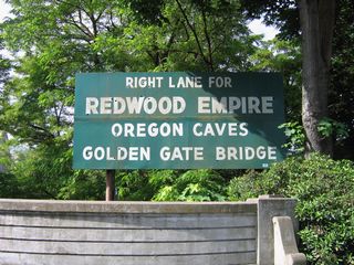 A vintage art deco sign at the Caveman Bridge references the destinations along the Redwood Highway, including the Redwood Empire, Oregon Caves National Monument, and the Golden Gate Bridge.