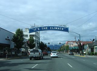 A decorative overhead sign preceding G Street on 6th Street welcomes all to Grants Pass: &quot;It&amp;apos;s the Climate.&quot;