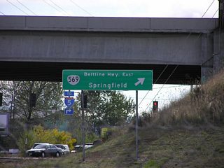 A folded diamond interchange (Exit 5) joins OR 99 with OR 569 (Randy Pepe Beltline) along the west Eugene city line. OR 569 is a freeway extending east to I-5 at the Springfield city line. This guide sign was replaced after 2011.