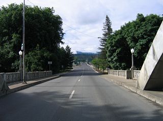 The Caveman Bridge spans a portion of Riverside Park ahead of the signalized intersection joining OR 99 (6th Street) with Park Street.