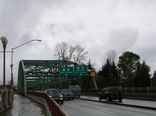 This suite of photographs displays the Ferry Street Bridge of Coburg Road over the Willamette River. The four lane truss bridge leads southward into the northern reaches of downtown Eugene. Overheads attached to the superstructure partition traffic for OR 99/126 Business for the University of Oregon, the Eugene central business district, and the Hult Center for the Performing Arts.
