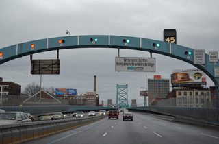 Interstate 676/U.S. 30 rise onto the Benjamin Franklin Bridge from 6th and Race Streets to cross the Delaware River. The suspension bridge accommodates seven overall lanes with a movable barrier and variable speed limits.
