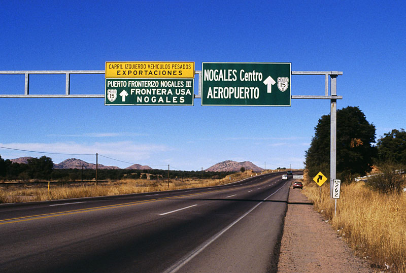 <i>Near the Mex. 15D split just south of Nogales. As the sign says, one branch goes to downtown Nogales (and the border crossing near where I-19 begins), while the other heads out west to what is called Nogales III on the Mexican side and Mariposa on the US side. The Mexican immigration and Customs station is actually a substantial distance south of the border and the length of the Mex. 15D expressway between the border and the border station is a closed "corredor fiscal," with high chain-link fences designed to prevent entry and exit. The fences do not stop trinket sellers, however. </i>