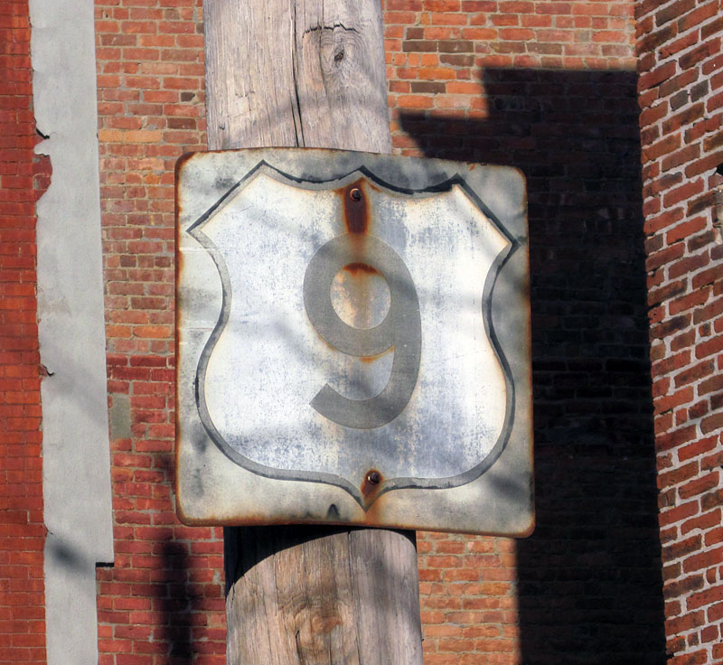 This shield was originally a white square with the outline shield, and then got repainted to a black square around 1961.  The repaint is clearly fading.