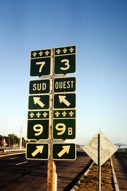 Laniel, Quebec. <br><br>
<i>This one really blew me away. These signs are similar to the Quebec shields today, green with three fleur-de-lis. However, the route numbers are those used before the great renumbering. My 1964 map shows names autoroutes, and the old Quebec road numbers. In 1967, numbered autoroutes have been introduced, but the old route numbers still retain on the non-freeway system. In 1972, 1973 and 1974, there was a mix: the new numbers were starting to be introduced but the main routes still had their old designation. I missed 1975, but 1976 had the full renumbering. This was a great find in my slides – kind of a transition period.</i>