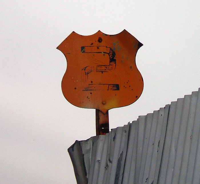 Old cutout US highway marker repainted to serve as a gate number identifier at a junkyard in Moses Lake.