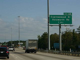 Cypresswood Drive and Holzwarth Road converge in a commercialized area adjacent to IH 45 at the ensuing exit.
