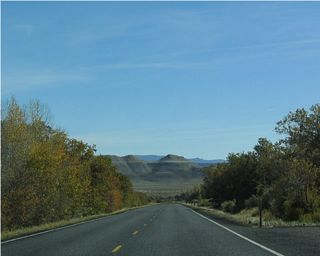 The topography of the land changes a bit as the highway lowers its elevation. Most of the bright red and orange hues found in the higher terrain around Red Canyon and Bryce Canyon have changed to a more neutral brown. However, some splashes of color may be found here, including Kodachrome Basin State Park.