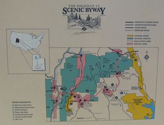 This roadside map shows the main attractions and parks along the length of the Utah 12 Scenic Byway at the rest area/pullout located just west of Red Canyon. From west to east, the attractions include Red Canyon/Dixie National Forest, Bryce Canyon, Kodachrome Basin State Park, Grand Staircase-Escalante National Monument, Escalante Petrified Forest State Park, and Capitol Reef National Park. This map is located at the rest area located on the south side of Utah 12 at the western entrance into Red Canyon.