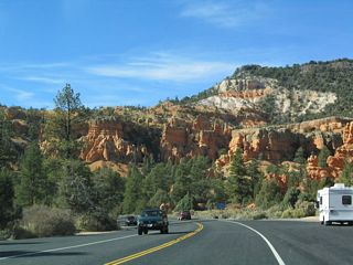 After passing through the two tunnels, Utah 12 passes by some beautiful red rock formations contrasted by the green trees and shrubs that surround it. In some of these high desert locations, the wettest part of the year may be during the summer, when afternoon thunderstorms become more common. Winter snows also bring moisture to the area. This is unlike the southern deserts of Southern California and Arizona, where such storms are less frequent.
